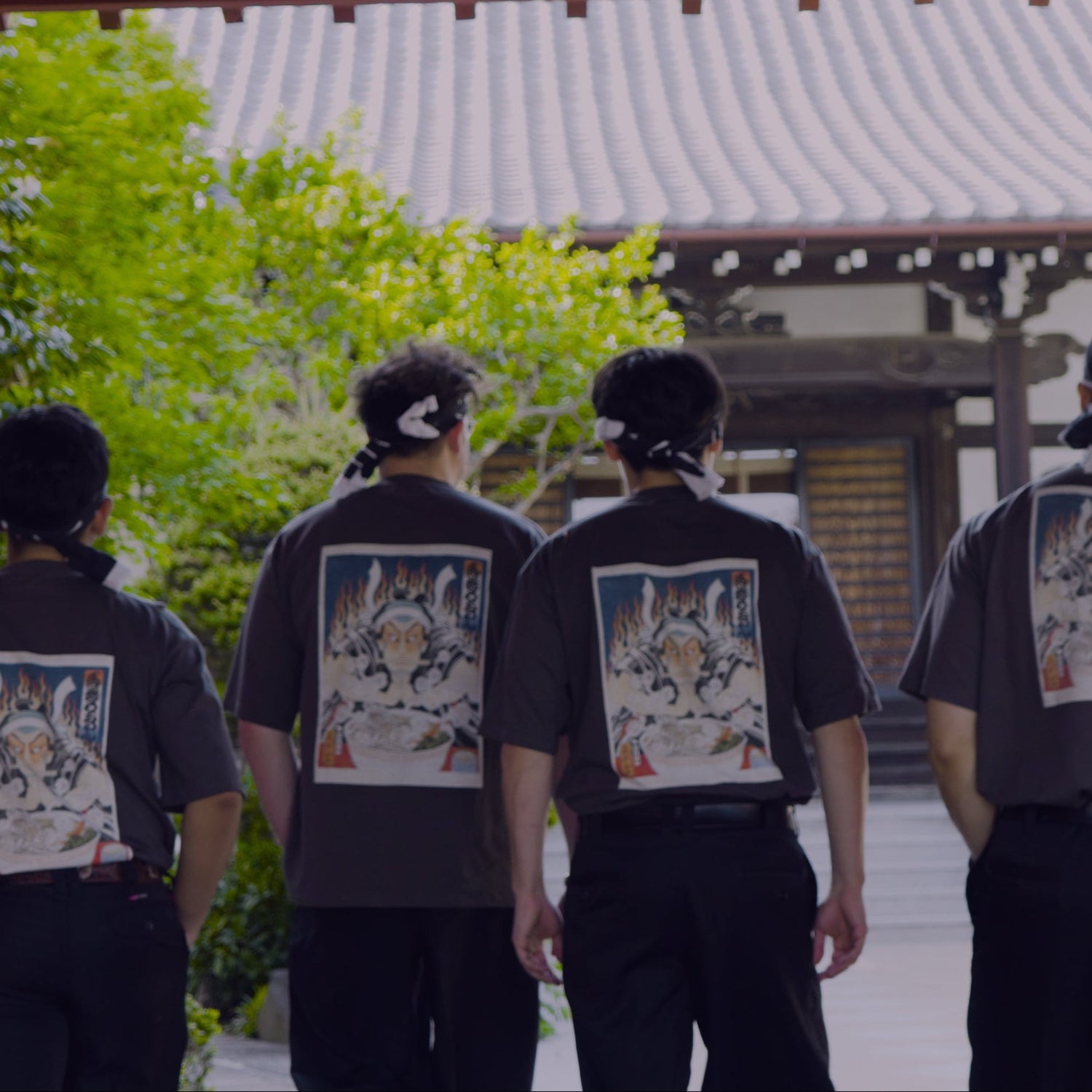 Four individuals wearing black t-shirts with graphic designs walking through a traditional Japanese gate.